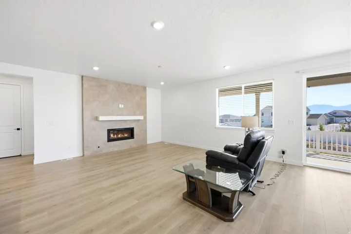 Spacious living area featuring light wood-finish flooring, recessed lighting, and a modern fireplace with a tile surround and white mantel