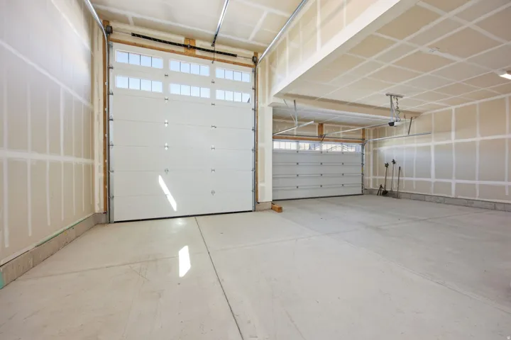 Three-car garage featuring concrete flooring, a large white garage door with upper window panels, a second garage door, and unfinished interior walls