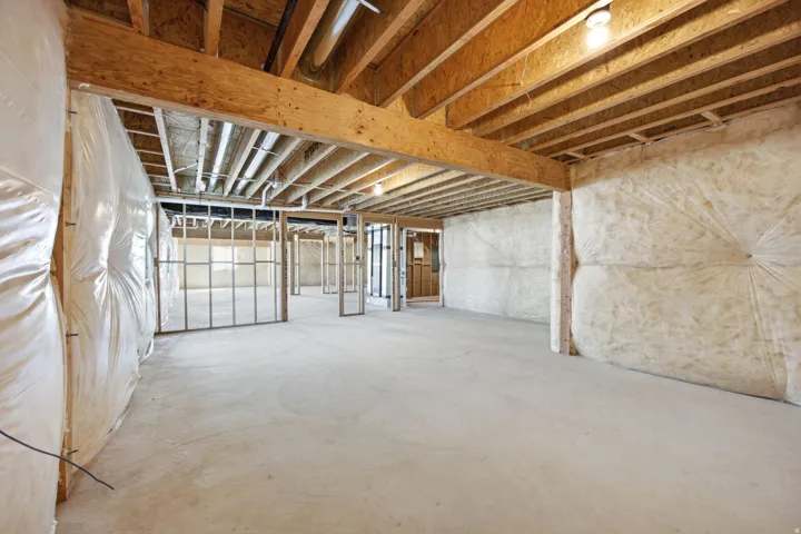 Expansive unfinished basement featuring exposed wood joists and structural beams, concrete flooring, insulated perimeter walls, and framed interior partitions, offering significant potential for customization