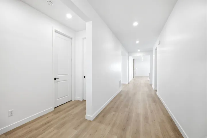 Bright interior hallway featuring wood-finish flooring, recessed lighting, and crisp white walls