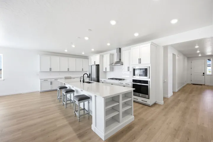 Open-concept kitchen featuring white shaker cabinetry, an expansive center island with integrated shelving, and stainless steel appliances