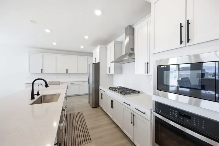Modern kitchen featuring white cabinetry, light-toned countertops, stainless steel appliances, a large island with an undermount sink, and wood-finish flooring