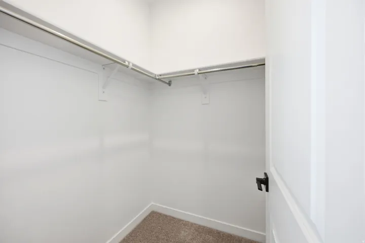 Walk-in closet with white walls, carpeted flooring, white baseboards, and built-in metal hanging rods