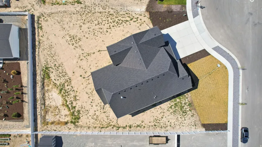 Newly constructed residence featuring a multi-pitched dark gray roof, an expansive undeveloped lot, and a concrete driveway