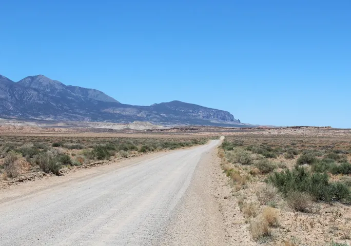 Unpaved road traversing expansive desert landscape under a clear blue sky, featuring distant mountains