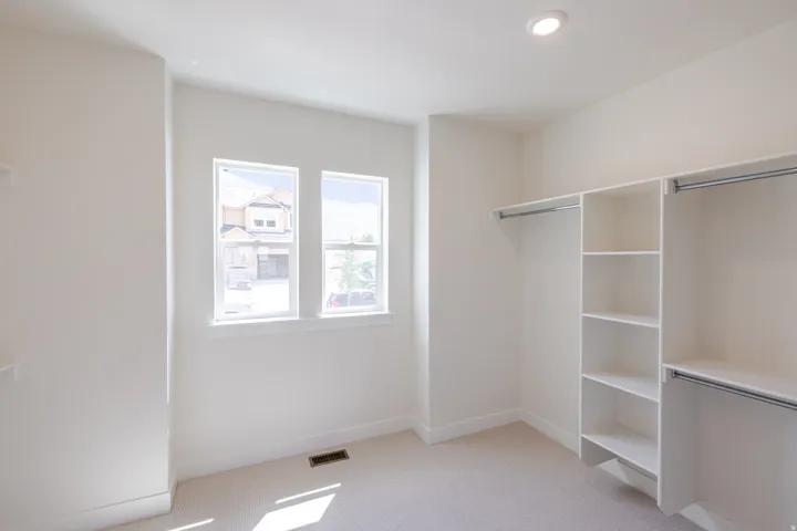 Recessed lighting illuminates this room featuring dual windows, light-toned carpeting, and built-in closet shelving