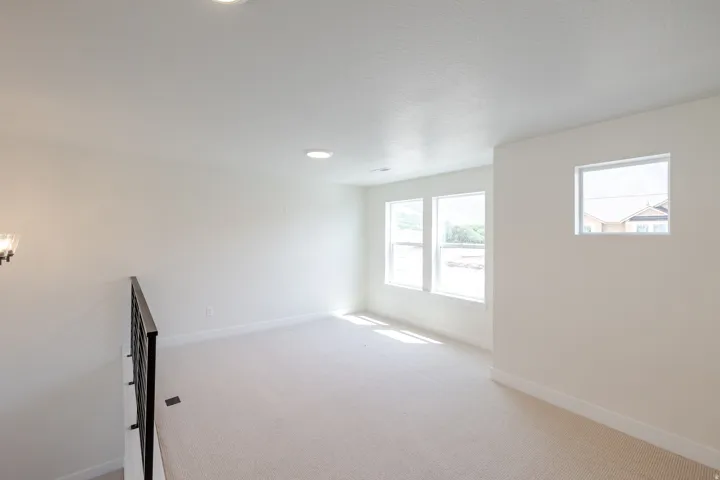 Carpeted loft area featuring a wrought iron railing, recessed lighting, and multiple windows