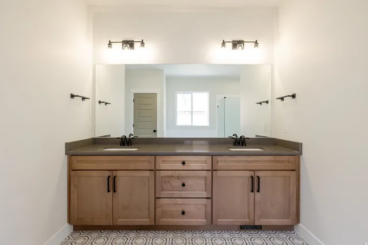 Dual vanity with wood-finish cabinetry, dark countertops, undermount sinks, and matte black fixtures