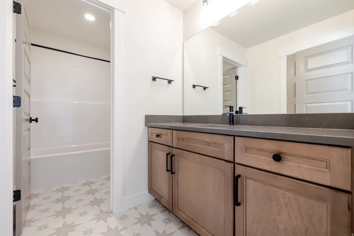 Bathroom featuring a dual-sink vanity with light wood cabinetry, a dark solid surface countertop, and matte black fixtures