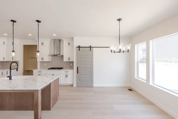 Modern kitchen and dining area featuring a large center island with a black faucet, white shaker cabinetry, stainless steel appliances, and pendant lighting
