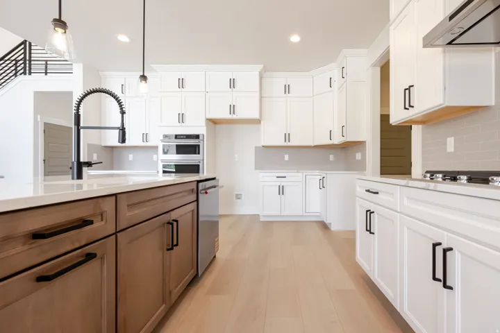 Light wood-finish flooring complements the two-tone cabinetry featuring white upper cabinets and a wood-finish island with black hardware