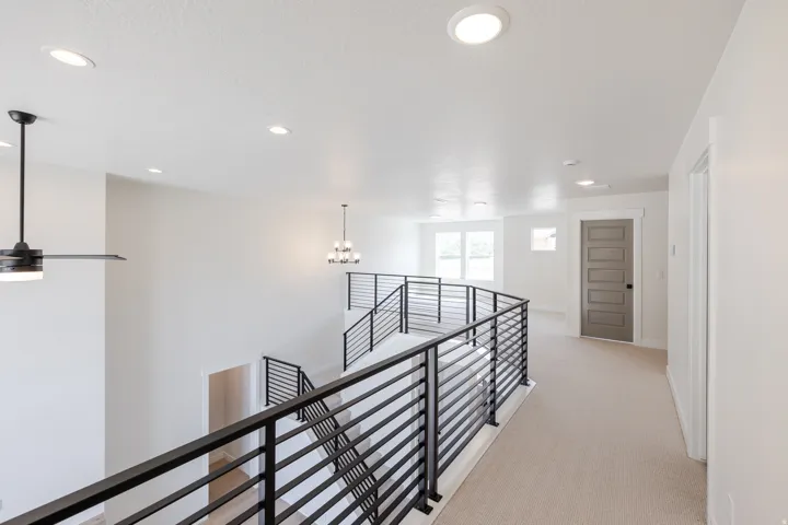 Carpeted upper-level hallway featuring modern black horizontal bar railings, recessed lighting, a contemporary ceiling fan, and a paneled interior door