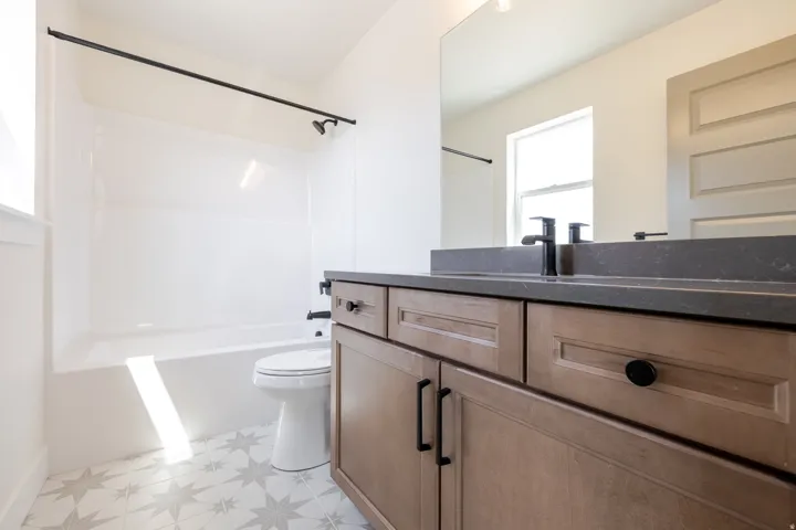 Bathroom featuring a tub/shower combination with matte black fixtures, a single vanity with wood-finish cabinetry, a dark countertop, and a large wall mirror