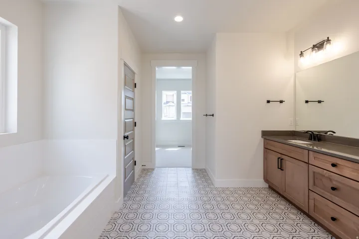 Bathroom featuring a built-in soaking tub with subway tile surround, patterned floor tiling, and a double vanity with stone countertop and integrated sink