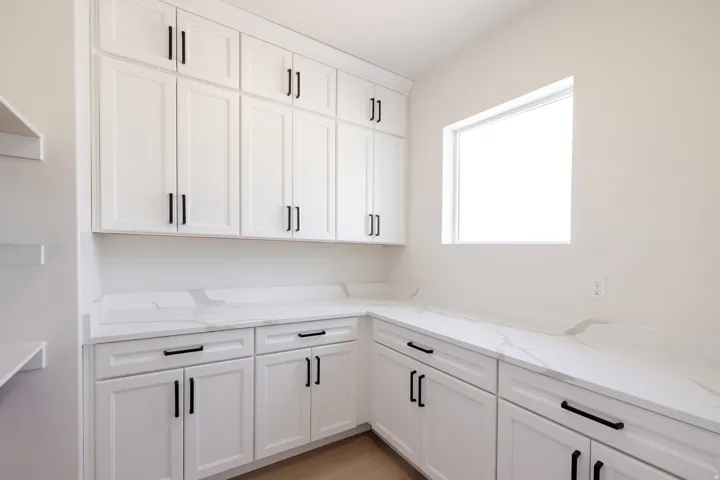Extensive white cabinetry with matte black hardware, white countertops with veining, and a flush-mounted window