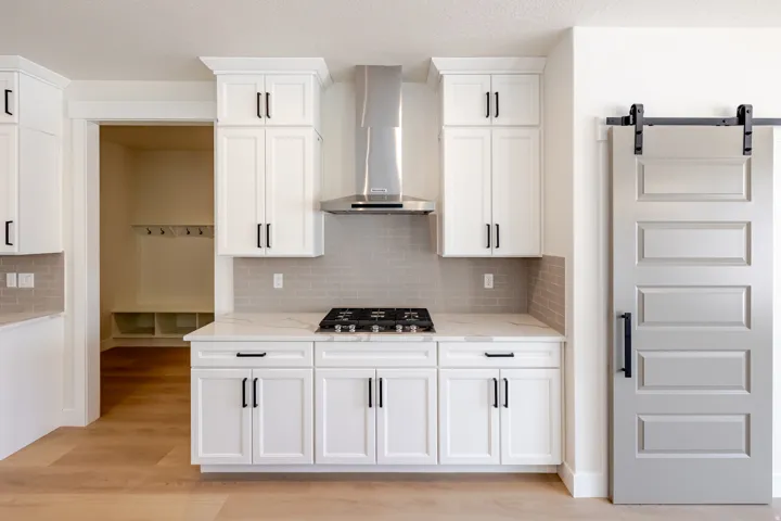 Modern kitchen featuring white shaker cabinetry, stainless steel range hood, stone countertops, and a gray subway tile backsplash