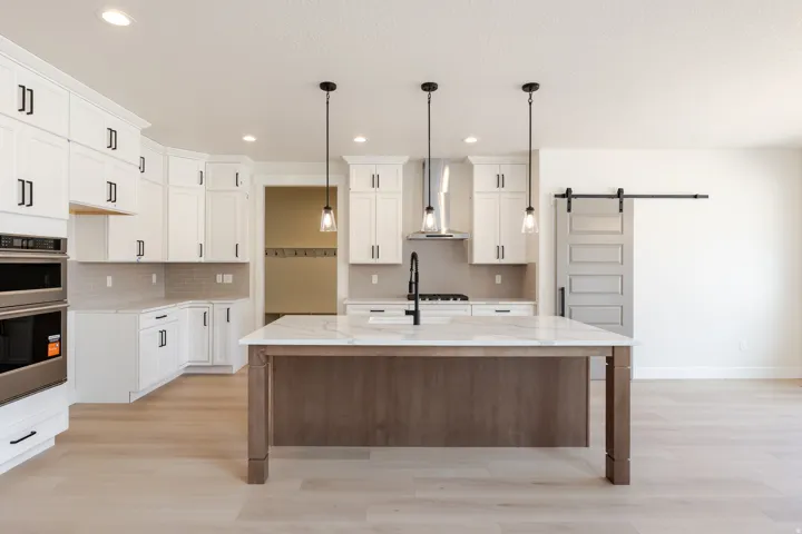 Modern kitchen featuring a large center island with a stone countertop, white cabinetry with matte black hardware, stainless steel appliances, and light wood-finish flooring