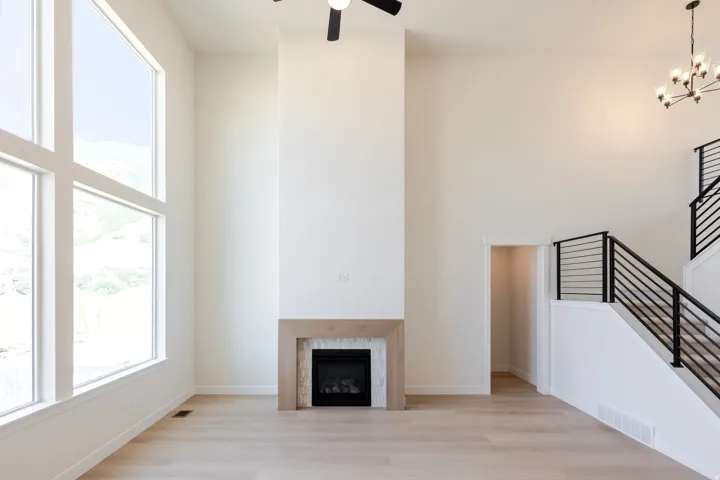 Spacious living area featuring high ceilings, light wood-finish flooring, a contemporary fireplace with a tiled surround and wood mantel, large multi-pane windows, and a modern staircase with black horizontal railings