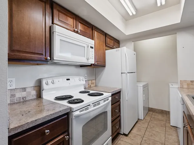 Kitchen featuring wood-finish cabinetry, white appliances, and a tiled backsplash