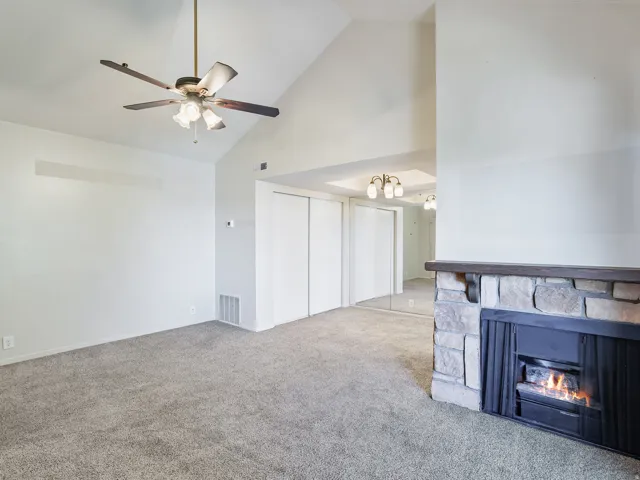 Living area featuring a stone fireplace with a wood-finish mantel, vaulted ceiling with a ceiling fan, and carpet flooring