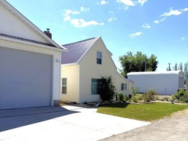 Property exterior featuring light-colored siding, a dark metal roof, and an attached garage with a gray door