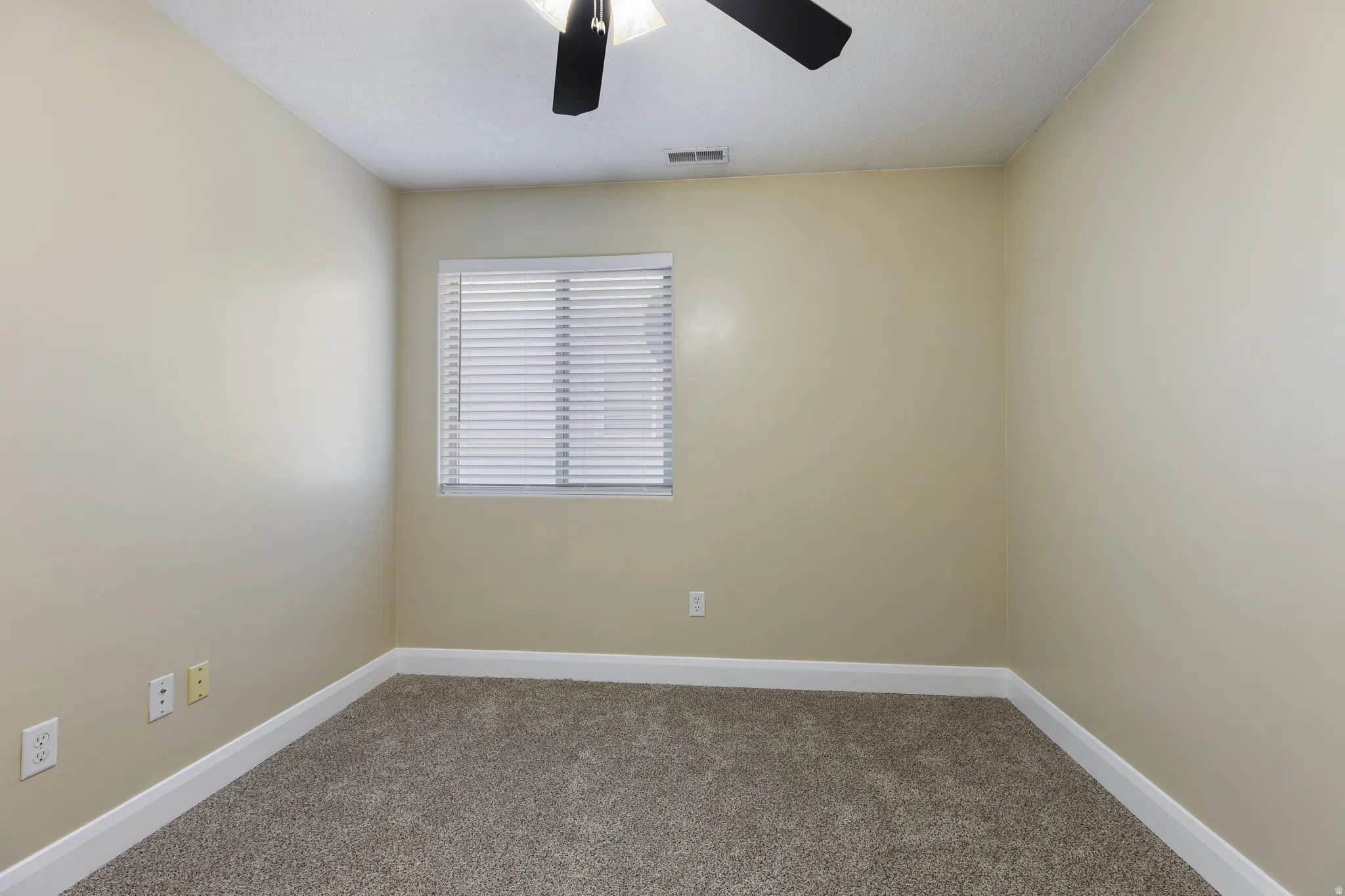 Neutral-toned room featuring a window with horizontal blinds, a ceiling fan, and light-colored carpeting