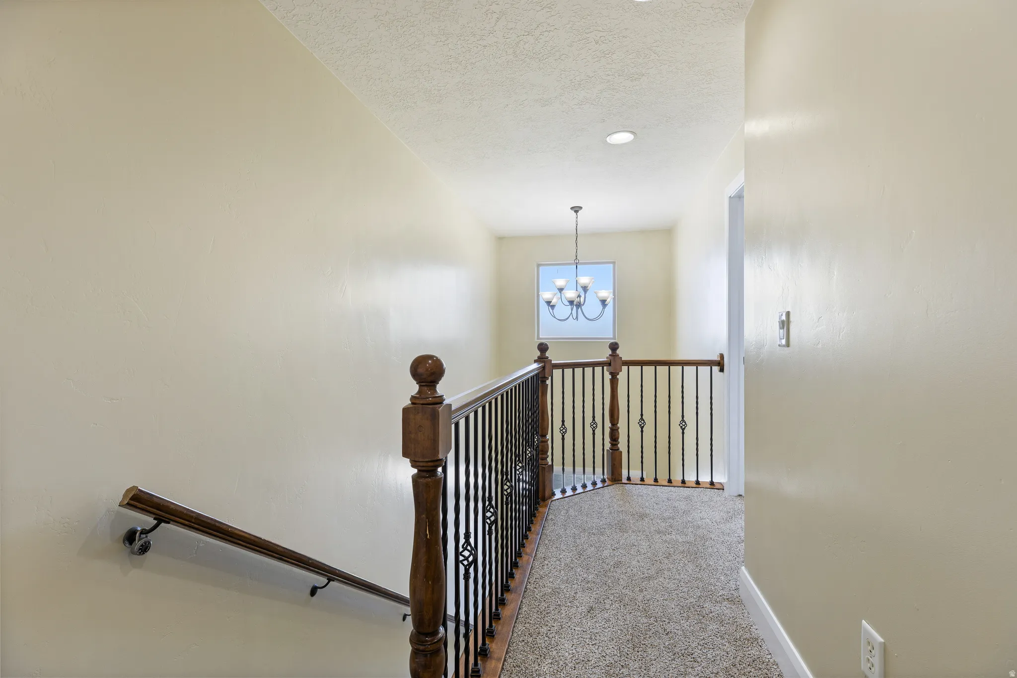 Upper-level landing featuring textured beige walls and neutral-toned carpeting