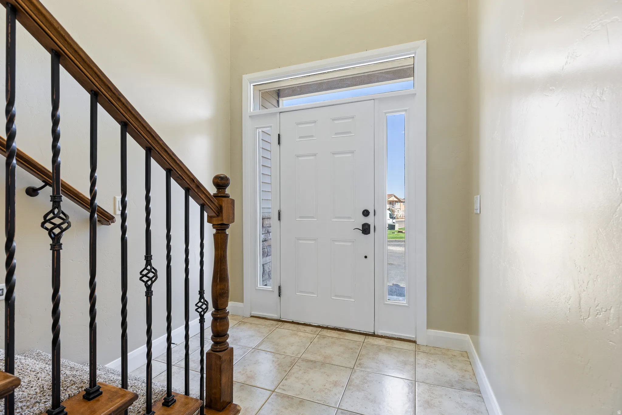 Entryway featuring a paneled front door with side lites and transom window, tile flooring, and a staircase with wood banister and wrought iron spindles