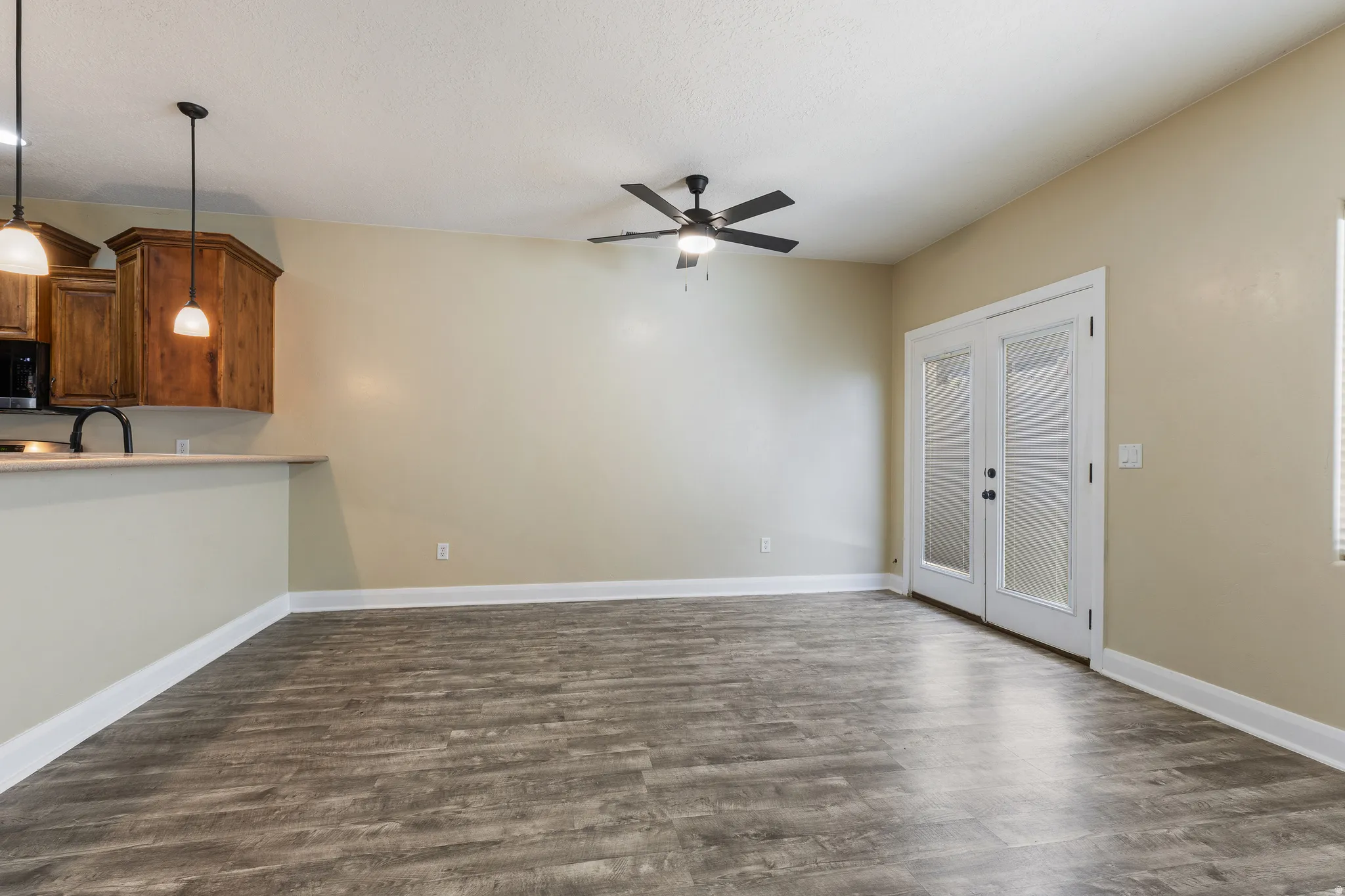 Spacious open-concept living area featuring wood-finish flooring, a ceiling fan, and light neutral wall paint