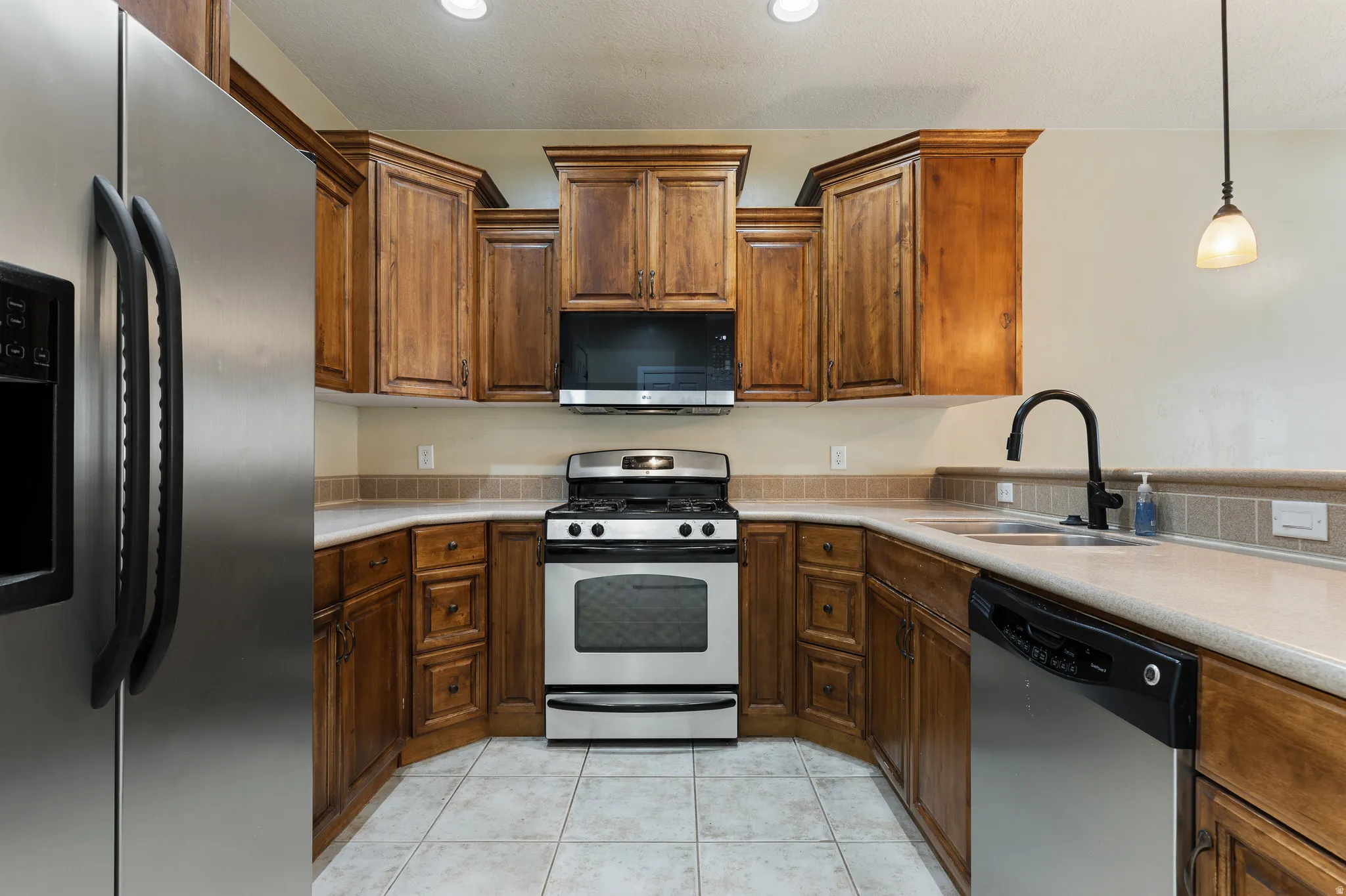 Kitchen featuring wood cabinetry, light-toned countertops, a stainless steel refrigerator, a stainless steel range with overhead microwave, and a stainless steel dishwasher