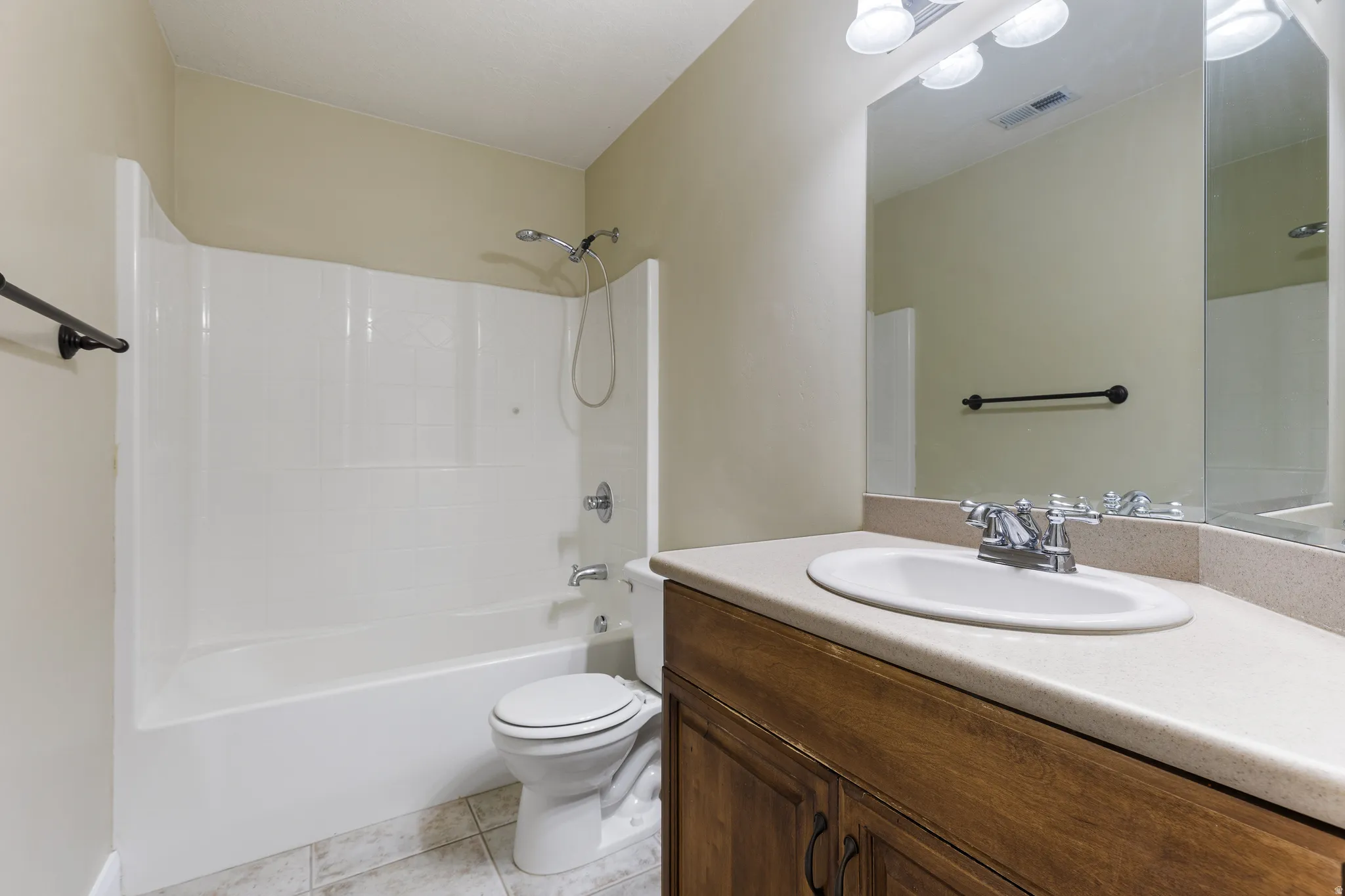 Bathroom featuring an integrated tub and shower unit, a wood-finish vanity with an oval sink, a light-toned countertop, a wall-mounted mirror, and tile flooring