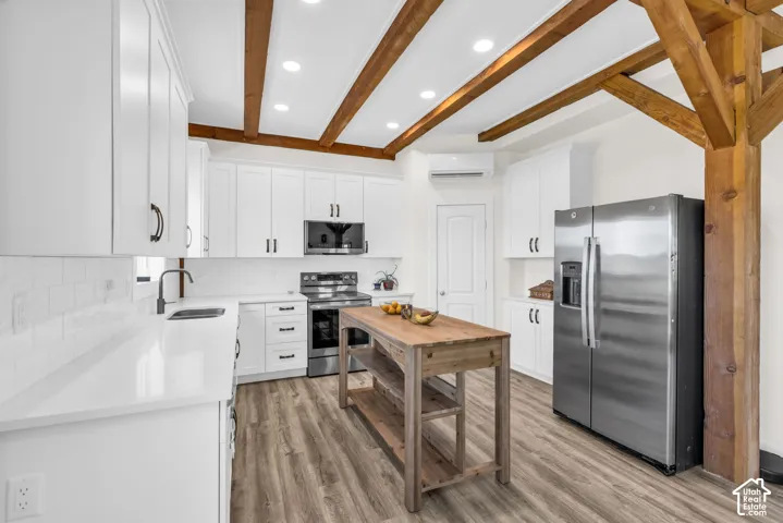 Kitchen featuring exposed wood beam ceilings, white cabinetry, integrated stainless steel appliances, wood-finish flooring, and a freestanding wood island