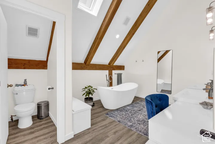 Vaulted ceiling bathroom featuring exposed wood beams and wood-finish flooring