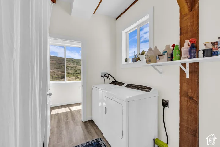 Laundry area featuring wood-finish flooring, a white-framed window, and exposed wood beams