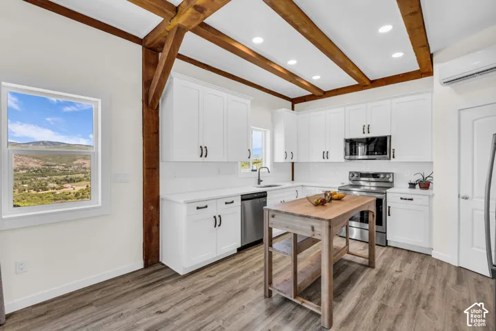Kitchen featuring exposed wood beams, white shaker-style cabinetry with matte black hardware, stainless steel appliances, and wood-finish flooring