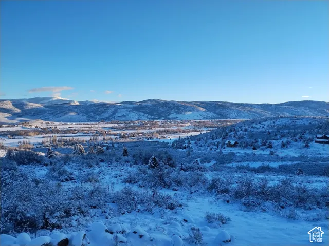 Expansive mountain landscape featuring snow-covered hillsides and distant peaks under a clear blue sky