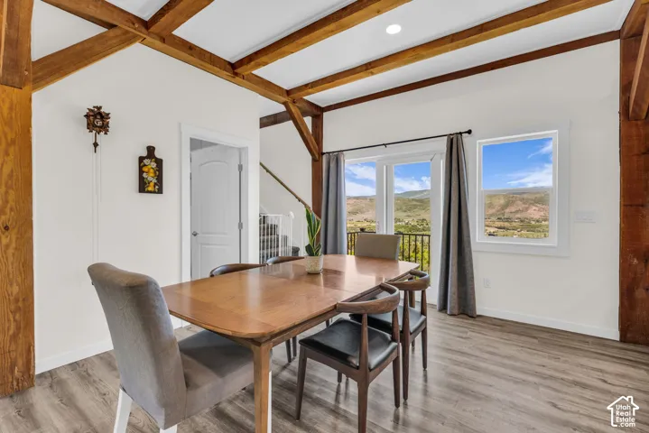 Dining area featuring exposed timber beams, wood-finish flooring, white walls, and a glass-paneled door opening to an exterior space with mountain scenery