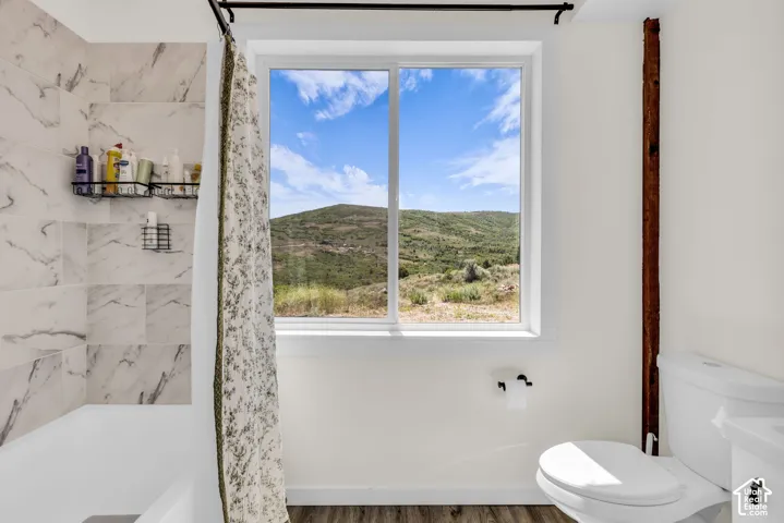 Bathroom featuring a tub/shower combination with marble-look tile surround, a white framed window, and wood-finish flooring