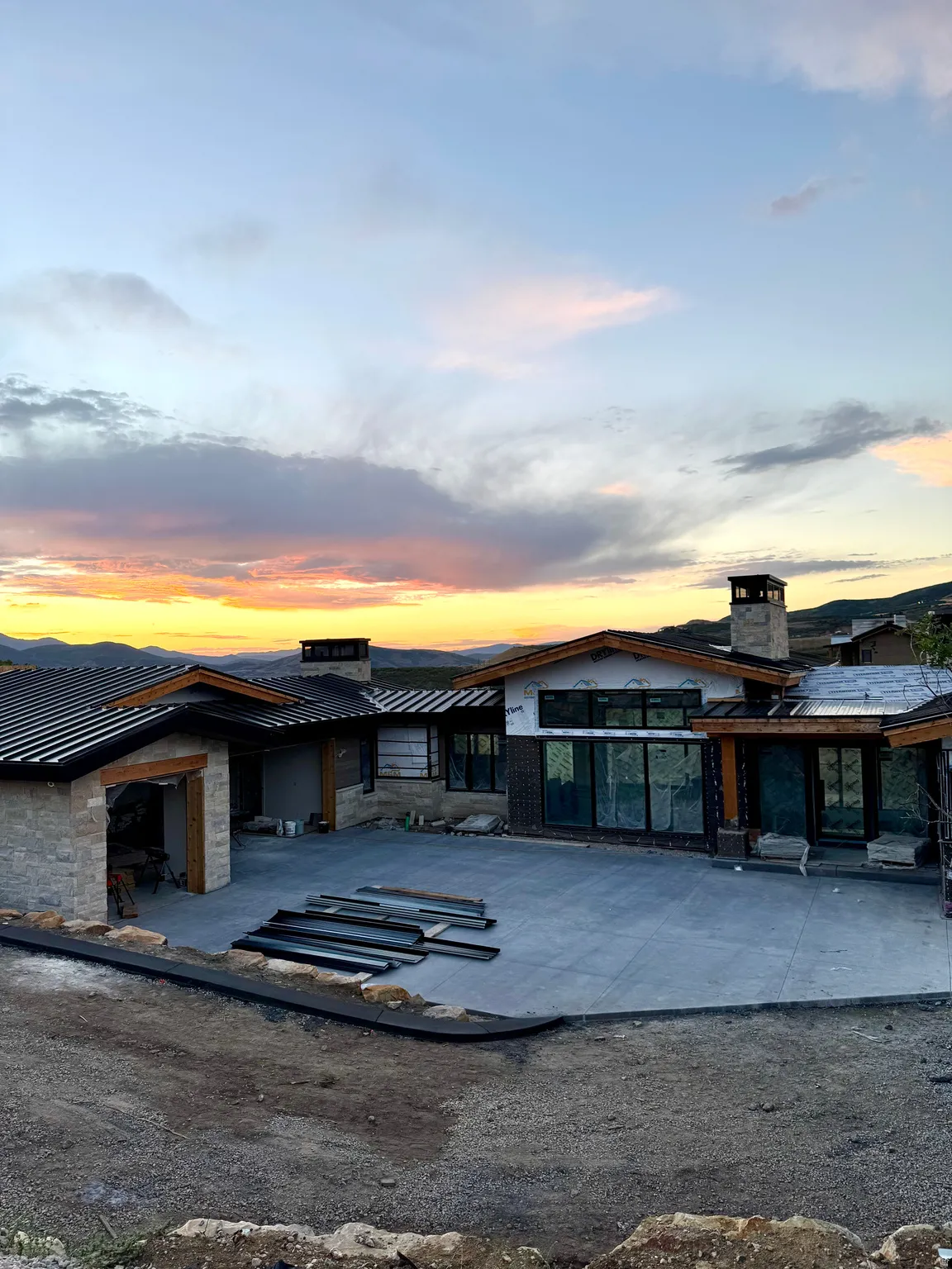 Stone exterior with wood accents, expansive concrete driveway, multi-pane windows, and a metal roof at sunset