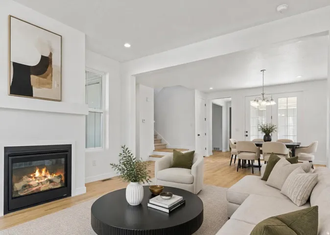 Virtually staged living area with a fireplace, light wood-finish flooring, and a dining area featuring double glass-paneled doors