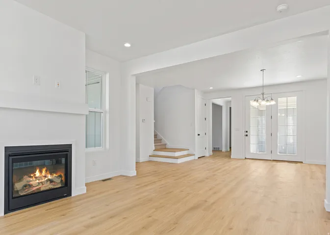 Spacious living area featuring a modern fireplace with a white mantel, light wood-finish flooring, recessed lighting, and a chandelier