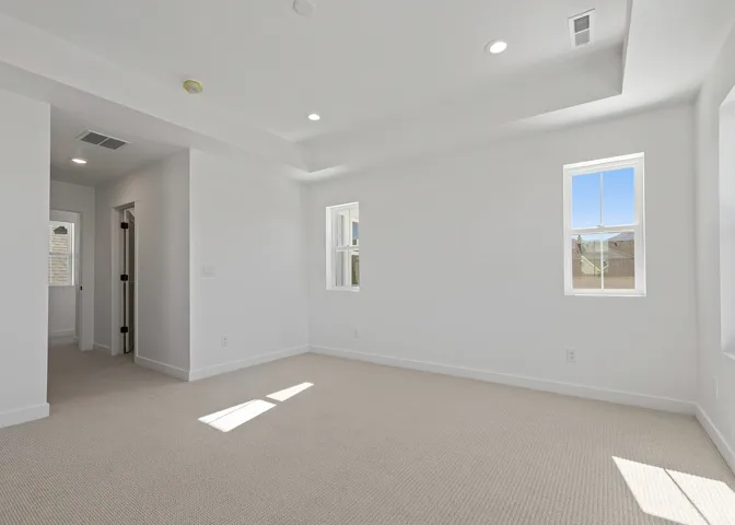 Spacious interior room featuring light-colored carpet flooring, recessed ceiling lighting, and a tray ceiling detail