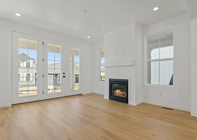 Bright living space featuring expansive wood-finish flooring, a contemporary fireplace with a white mantel, and recessed lighting