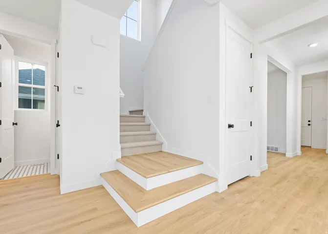 Entryway featuring light wood-finish flooring, white walls, and a staircase with carpeted treads