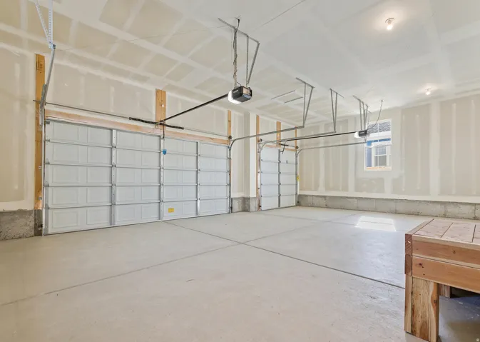 Spacious two-car garage featuring a concrete floor, automatic door openers, a window, and overhead lighting