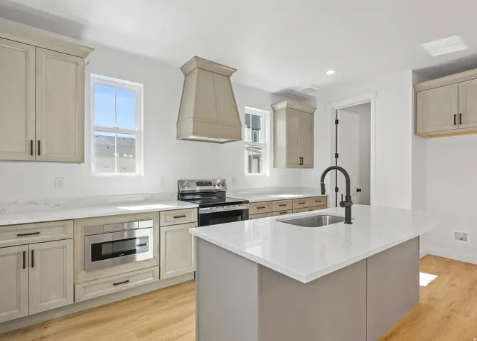 Modern kitchen featuring light wood-finish cabinetry, white countertops, an integrated stainless steel microwave, a black range, and a kitchen island with a matte black faucet