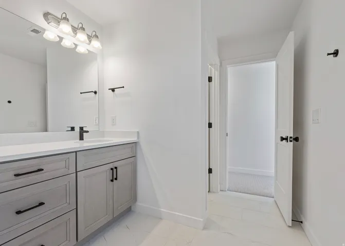 Bathroom vanity featuring light-toned cabinetry, a white countertop, and a single undermount sink with a matte black faucet