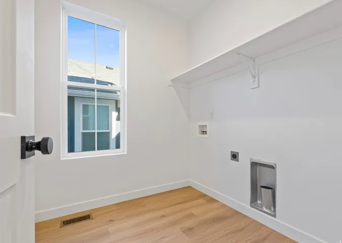 Dedicated laundry space featuring wood-finish flooring, a white trim window, built-in shelving, and utility hookups