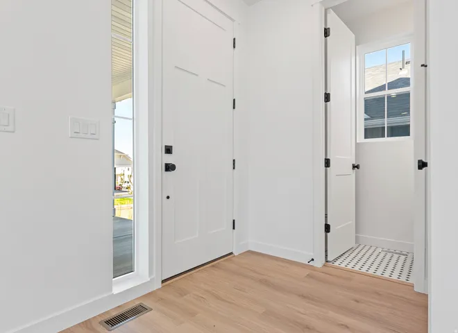 Entryway featuring a solid panel door with black hardware, wood-finish flooring, a sidelight window, and a utility space with a window and mosaic tile flooring