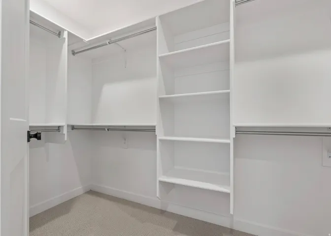 Walk-in closet featuring built-in shelving, multiple hanging rods, white trim, and light-toned carpeting